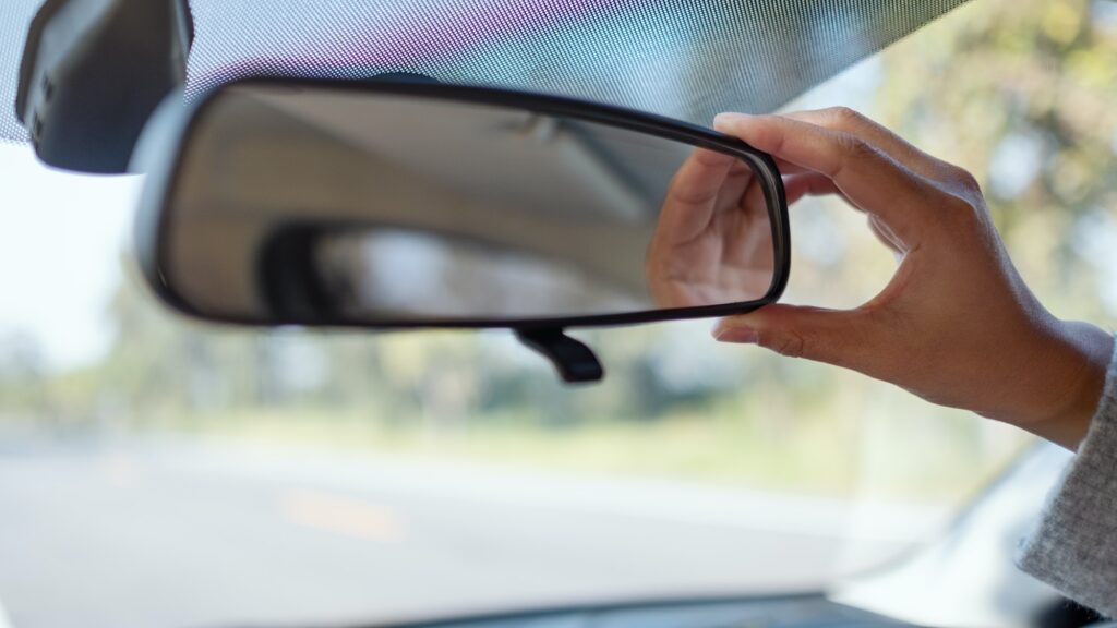 A woman adjusting a rear view mirror while driving car | Mastering Mirror Usage for a Successful K53 Driving Licence Test