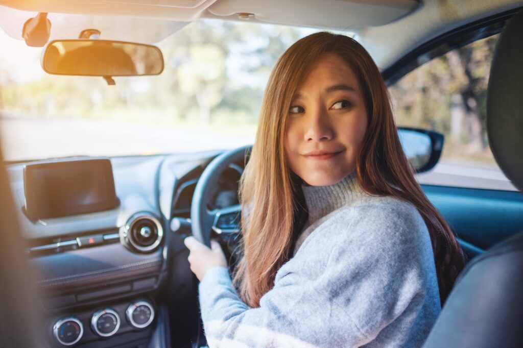 A woman holding steering wheel and looking back while driving in reverse on the road |  Mastering Straight-Line Reverse: A Crucial Skill for the K53 Driving Licence Test