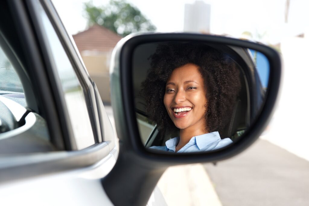 Reflection in side mirror of smiling African woman driving car | Mastering Mirror Usage for a Successful K53 Driving Licence Test