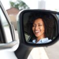 Reflection in side mirror of smiling African woman driving car | Mastering Mirror Usage for a Successful K53 Driving Licence Test