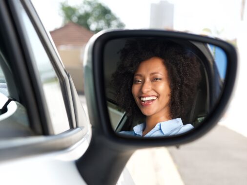 Reflection in side mirror of smiling African woman driving car | Mastering Mirror Usage for a Successful K53 Driving Licence Test