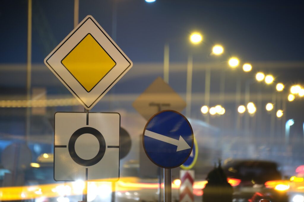 Roundabout road signs with blurred cars on city street traffic at night. Urban transportation | K53 Information Signs | Pass Your Learners Licence in South Africa 