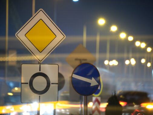 Roundabout road signs with blurred cars on city street traffic at night. Urban transportation | K53 Information Signs | Pass Your Learners Licence in South Africa